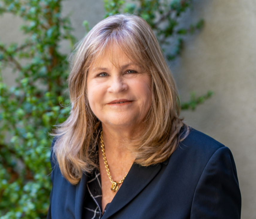 A woman in a suit and necklace standing outside.