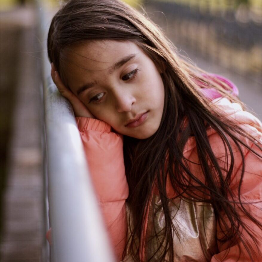 A young girl leaning against the railing of a bridge.